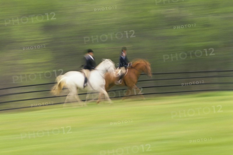 Two people riding on horses on field, blurred motion. Photographe : Stewart Cohen
