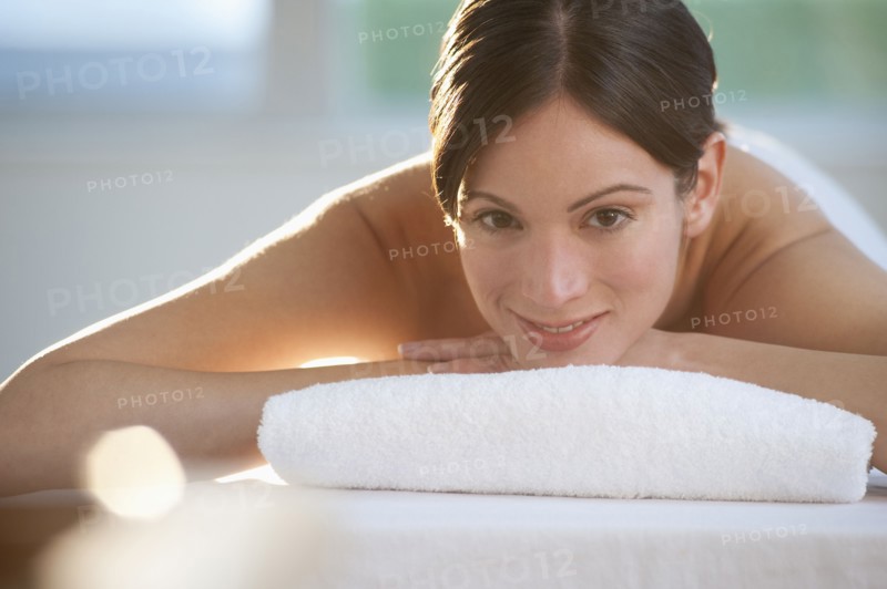 Mid-adult woman lying on massage table with candle in foreground.