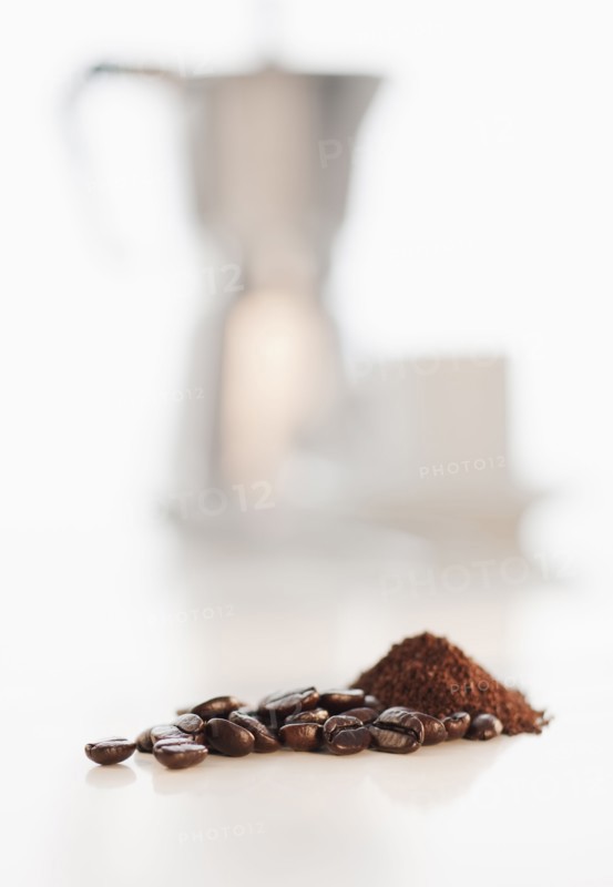 Heap of coffee beans with coffee cups in background.