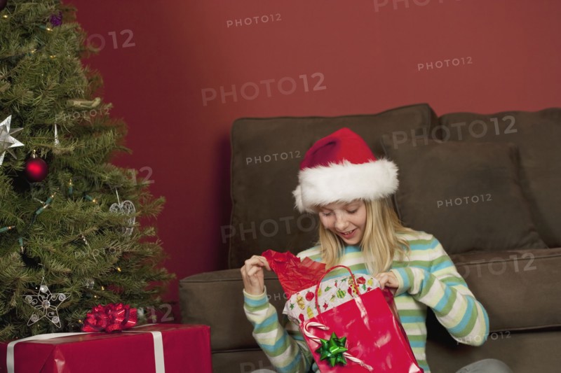 Teenage girl (13-15) wearing Santa hat opening Christmas gift. Photographe : Sarah M. Golonka