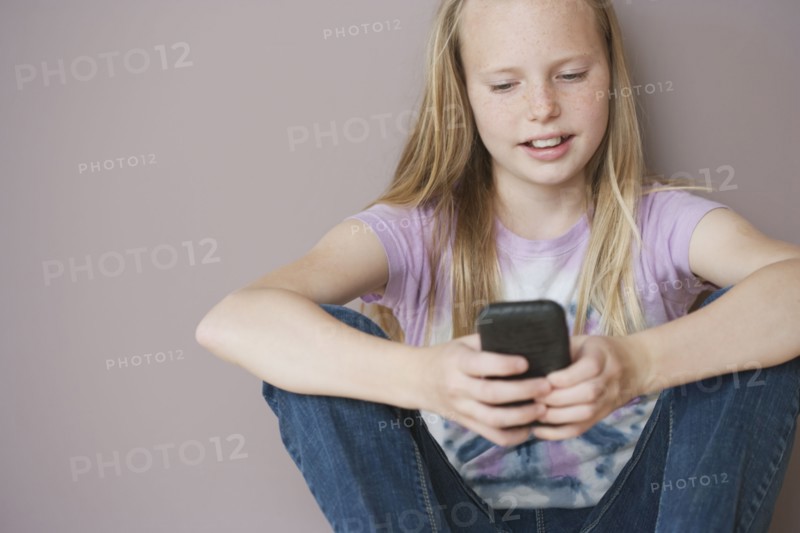 Girl (10-12) sitting and text messaging. Photographe : Sarah M. Golonka