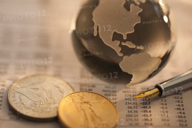 A globe on business papers with some coins.