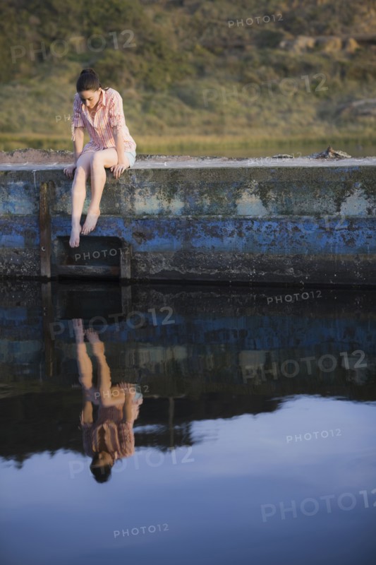 A woman sitting on a stone wall by water