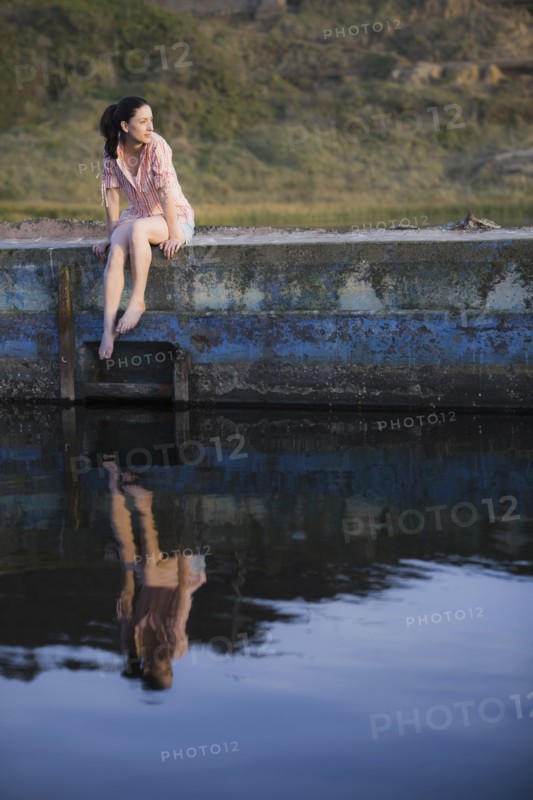 A woman sitting on a stone wall by water