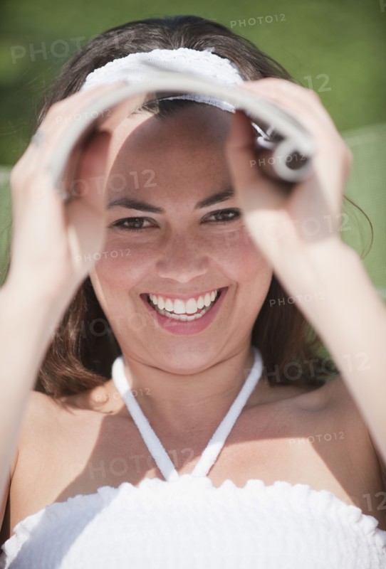 A woman outdoors shielding her eyes with a magazine.