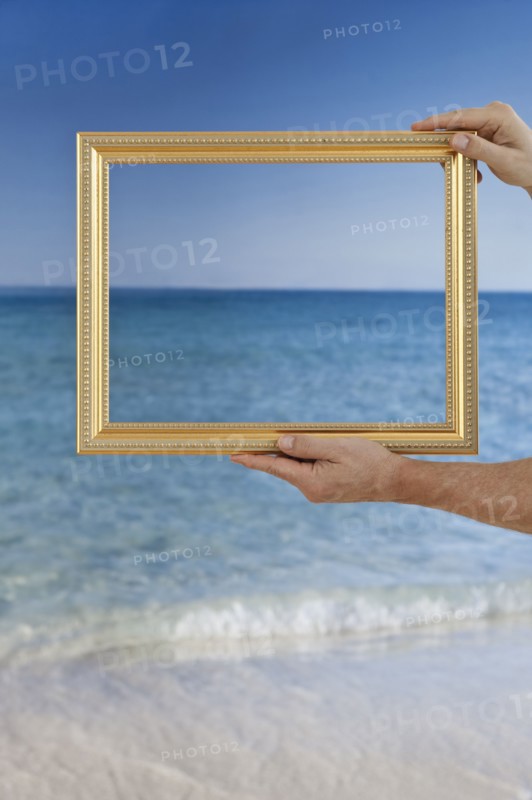 Hands holding a picture frame at a beach.