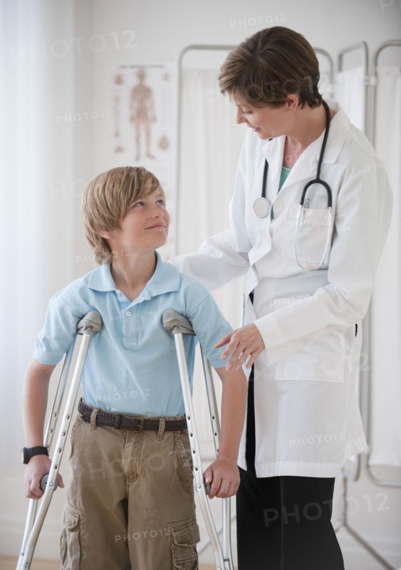 Female doctor assisting boy on crutches.