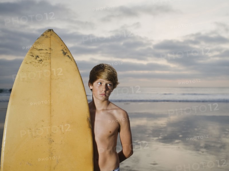 Boy standing beside surfboard