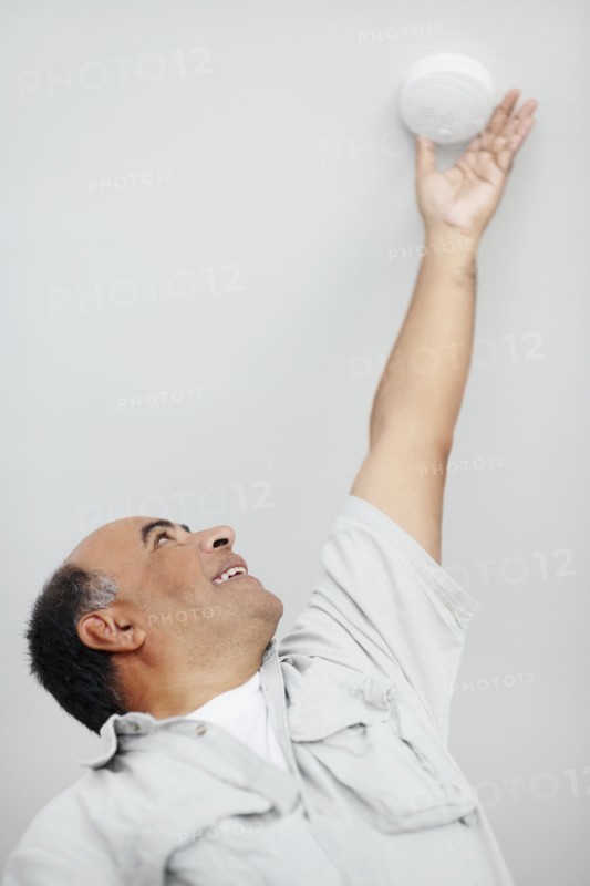 Man reaching up to smoke detector. Photographer: momentimages