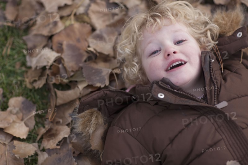 Young girl lying down on leaves. Photographer: Dan Bannister