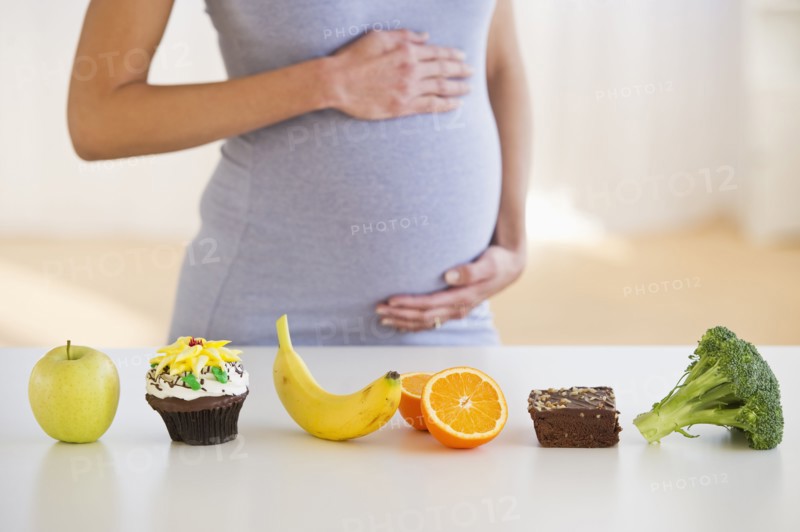 Pregnant woman standing behind a row of food.