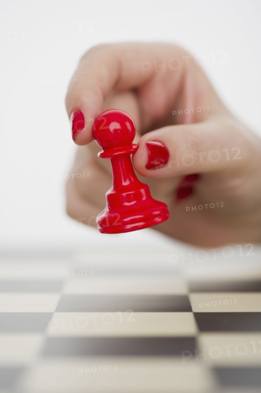 Hand holding red pawn chess piece.