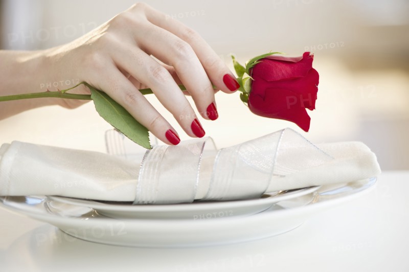 Hand putting a red rose on a place setting.