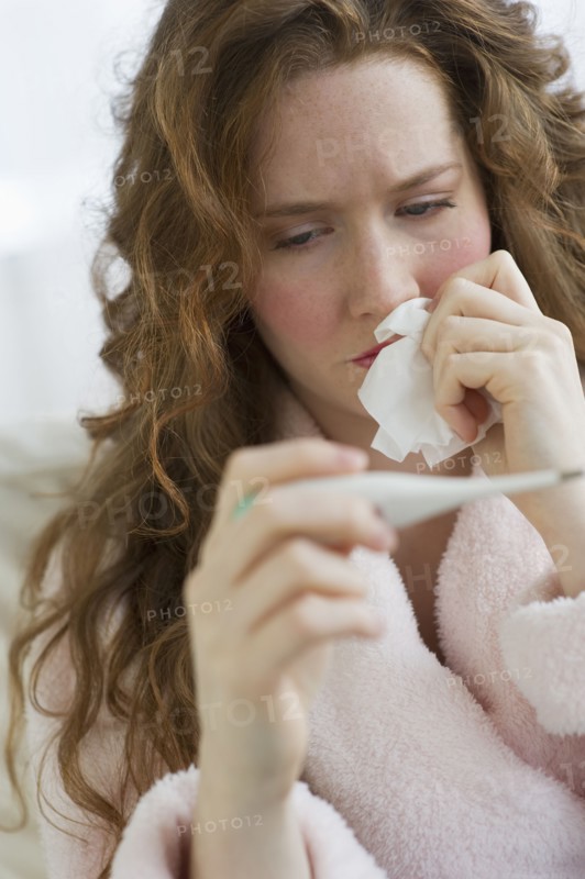 Sick woman looking at thermometer.