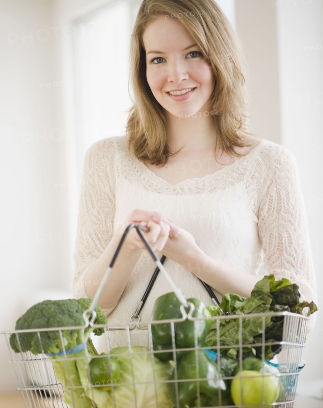 Woman holding basket of green vegetables. Photographe : Jamie Grill