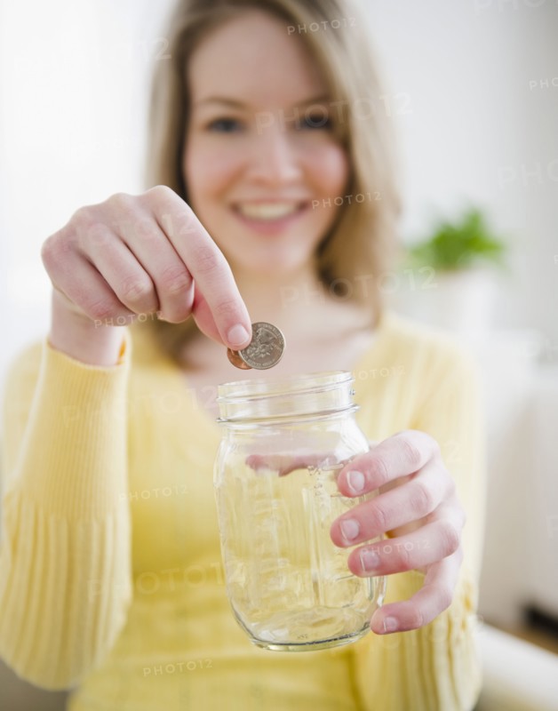 Woman putting coins in a jar. Photographe : Jamie Grill