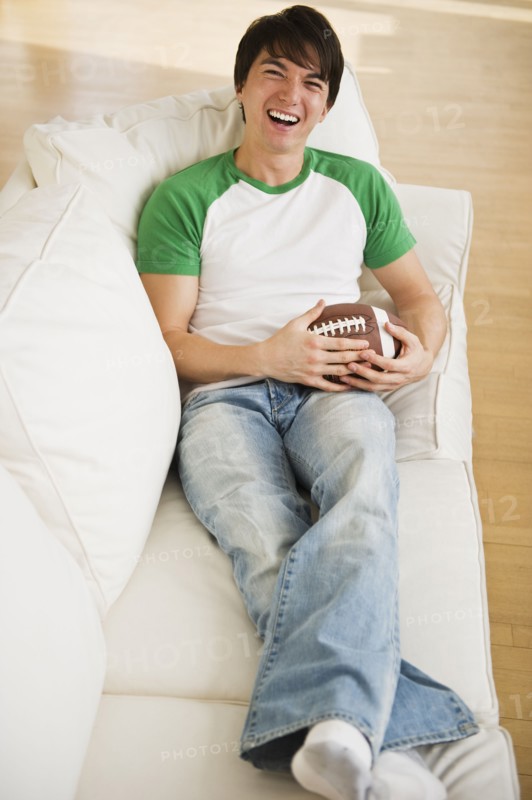 Male football fan relaxing on couch. Photographe : Daniel Grill