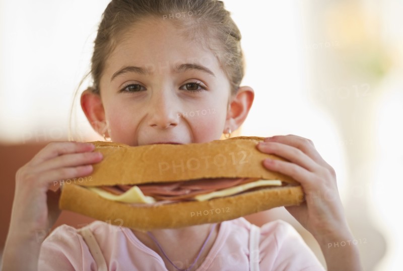 Young girl eating a large sandwich. Photographe : Daniel Grill