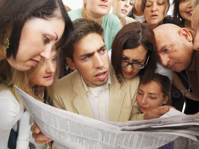 Group of people reading one newspaper. Photographe : momentimages
