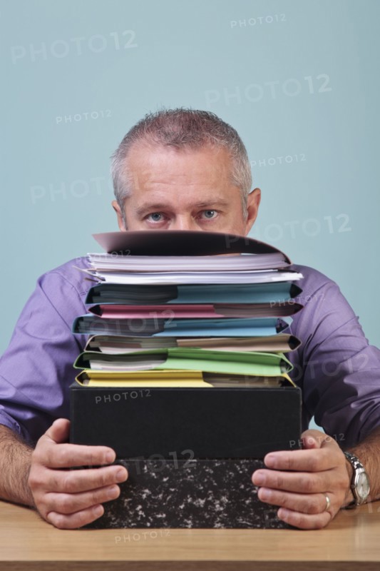 Man sitting behind a stack of paper work. Photographe : RTimages