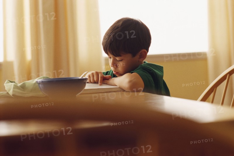 Young boy reading at the kitchen table. Photographe : Rob Lewine
