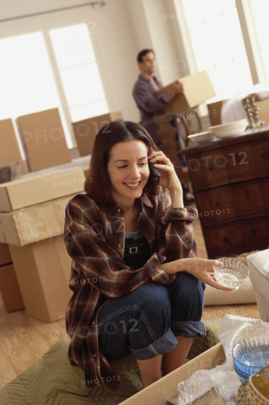 Woman talking on the phone while unpacking boxes. Photographe : Rob Lewine