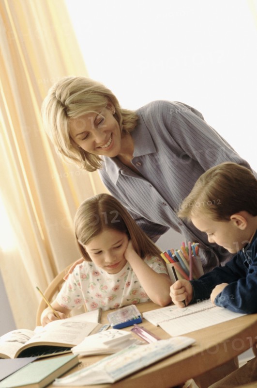 Mother watching her children coloring at the kitchen table. Photographe : Rob Lewine