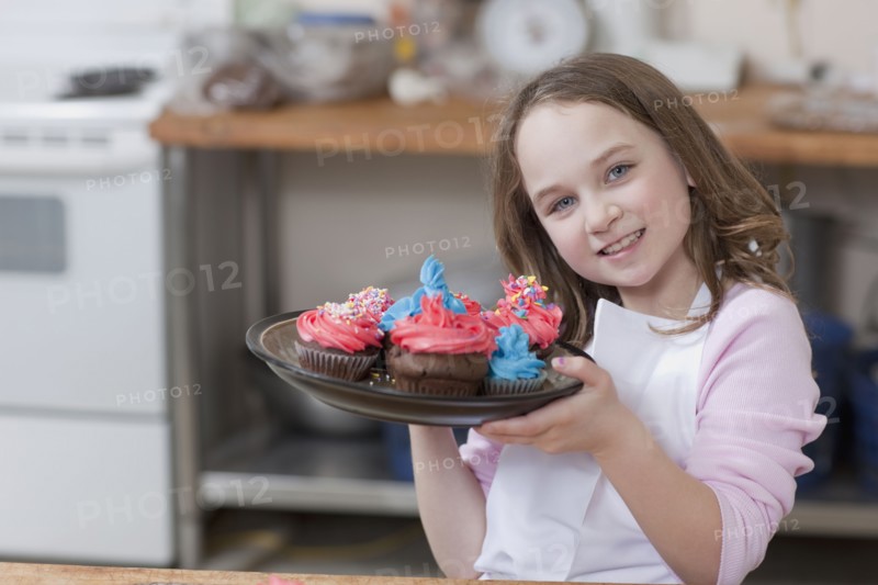Young girl holding a plate of cupcakes. Photographe : Dan Bannister
