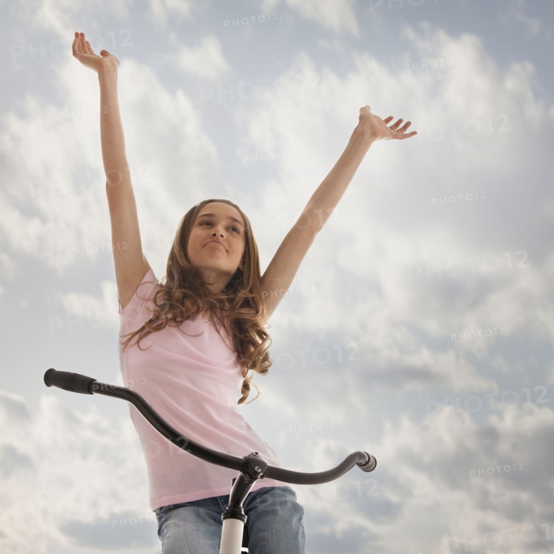 Pretty teenage girl with her arms raised while sitting on bike. Photo : Mike Kemp