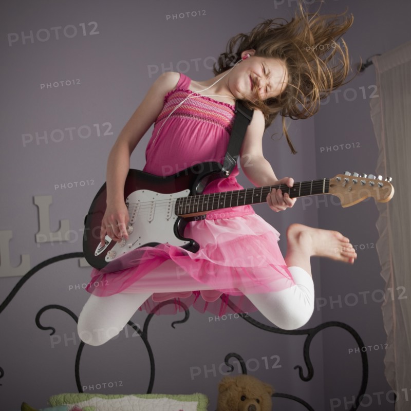 Young girls playing guitar on her bed. Photo : Mike Kemp