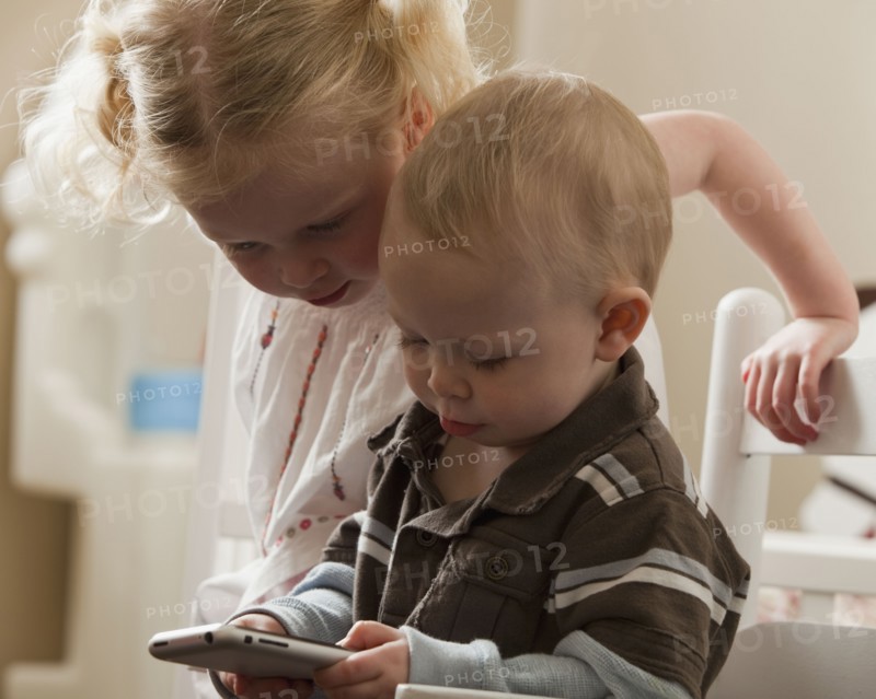Young siblings looking at cell phone together. Photo : Mike Kemp