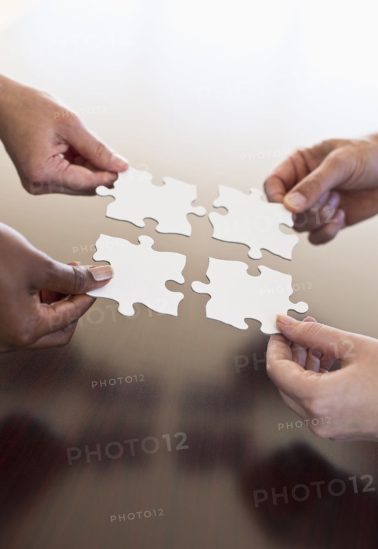 Four hands holding puzzle pieces.