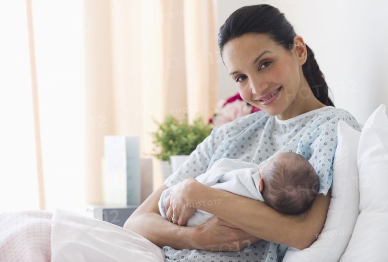 Mother holding newborn baby in hospital bed.