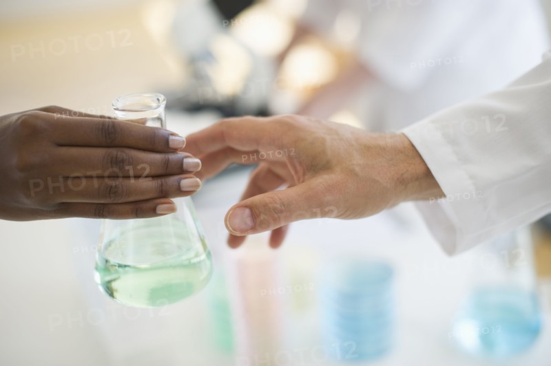 Hand passing beaker to another hand.