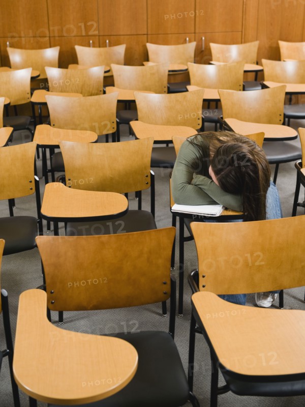 College student sleeping in empty lecture hall.