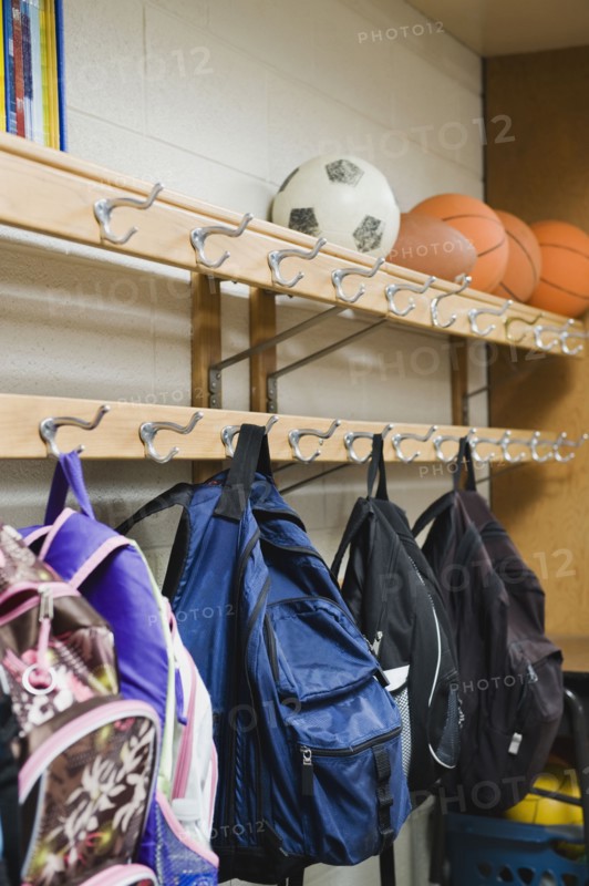 Children's backpacks hanging on hooks in classroom.