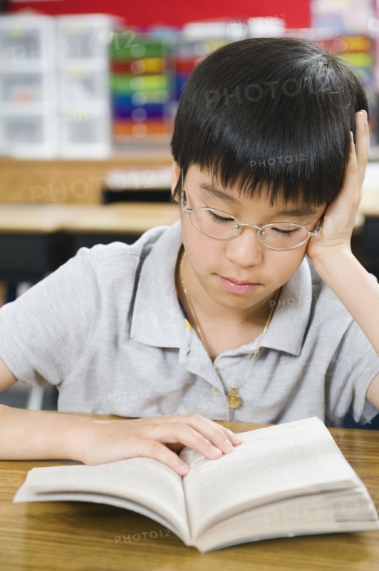 Elementary school student reading book at desk.