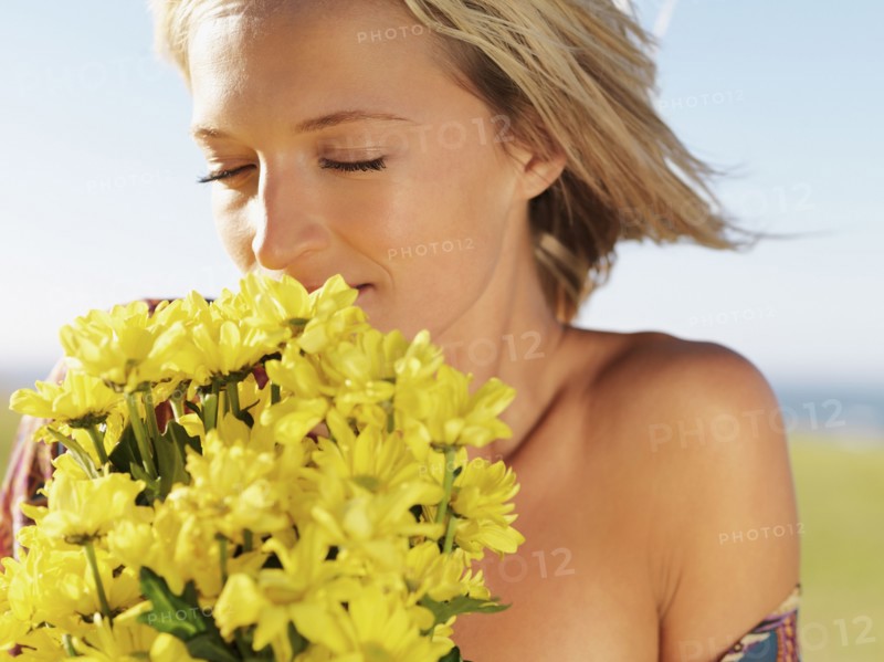 Blond woman smelling yellow flowers. Photo : momentimages