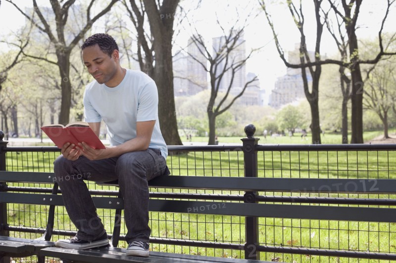 Man sitting on bench reading book in Central Park. Photo : David Engelhardt