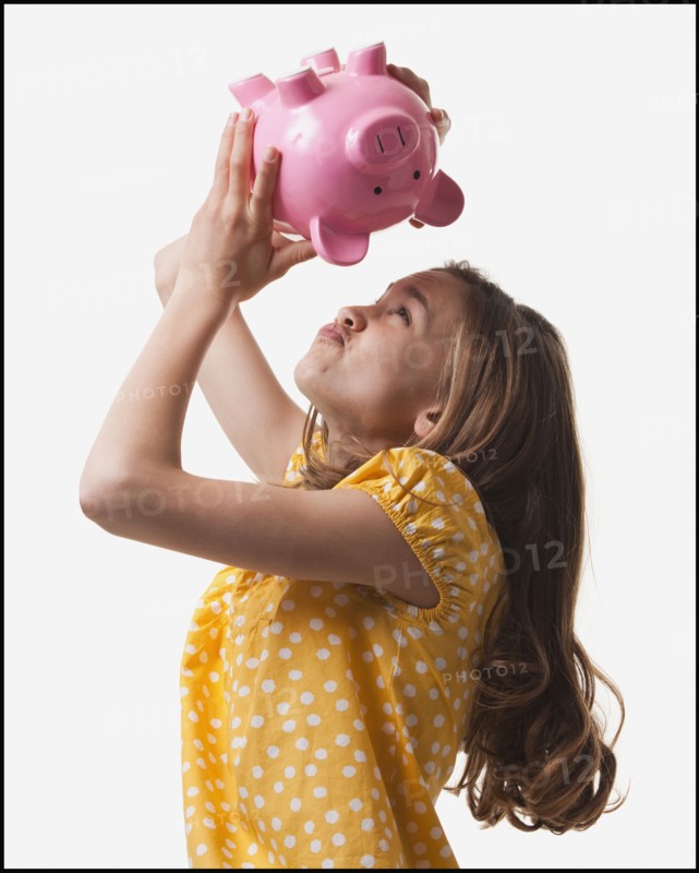Teenage girl trying to get money out of piggy bank. Photo : Mike Kemp