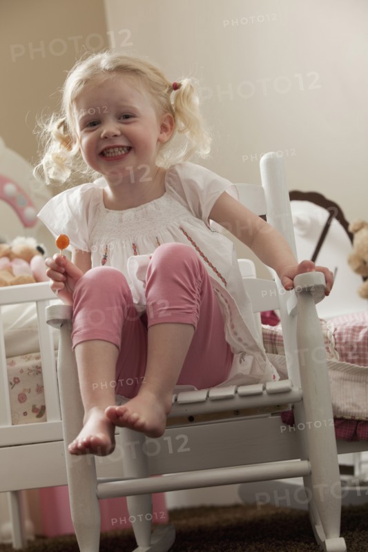 Young girl in rocking chair eating a sucker. Photo : Mike Kemp