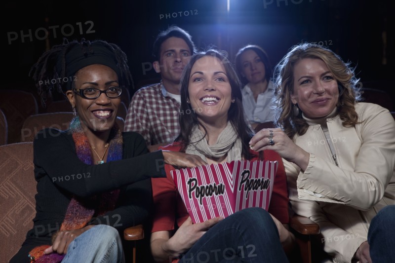 Three woman sharing popcorn in movie theatre. Photo : Dan Bannister
