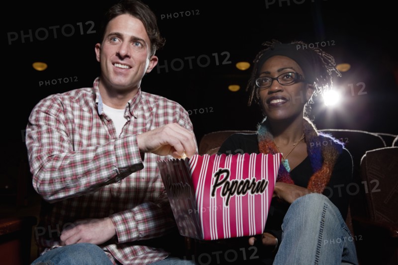 Couple eating popcorn in movie theatre. Photo : Dan Bannister