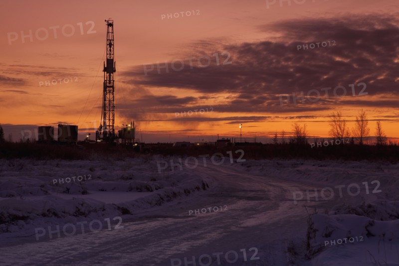 Snowy road at dusk with oil drilling rig in background. Photo : Dan Bannister