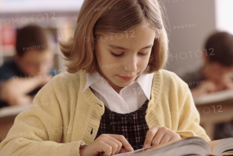 Elementary school student reading book at her desk. Photo : Rob Lewine