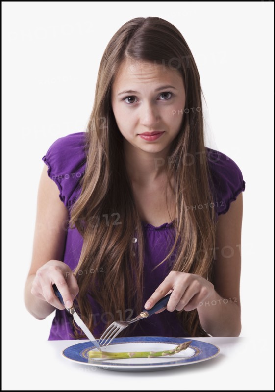 Unsatisfied teenage girl cutting a spear of asparagus. Photo : Mike Kemp