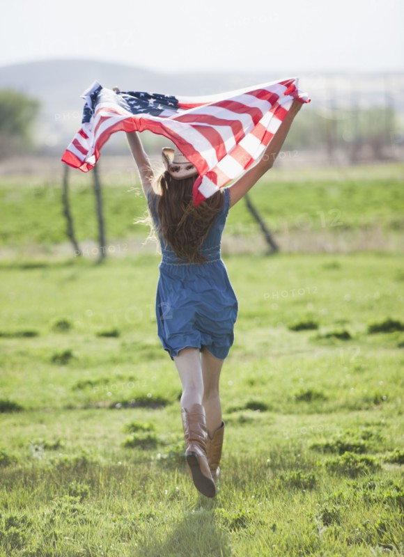 Beautiful cowgirl running with American flag in her arms. Photo : Mike Kemp