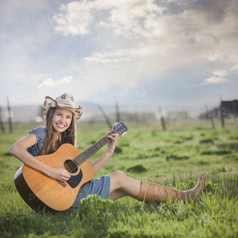 Cowgirl sitting in field playing guitar. Photo : Mike Kemp