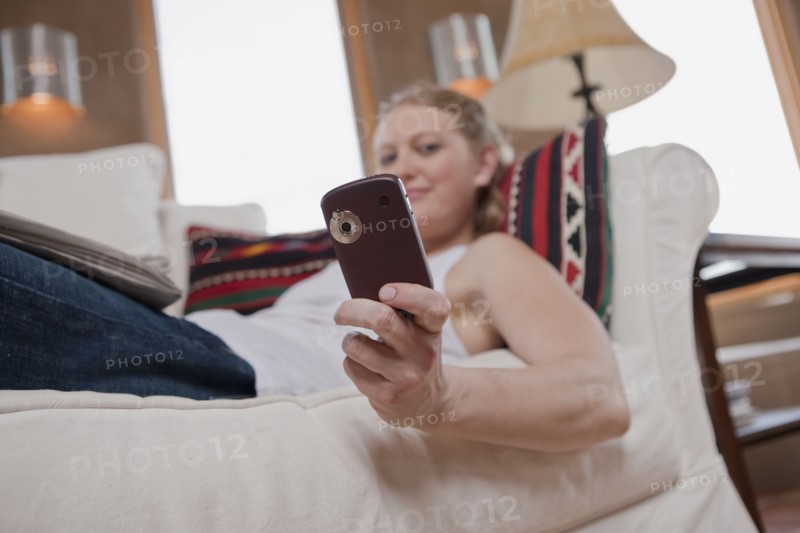 Woman relaxing on sofa while looking at cell phone. Photo : Dan Bannister
