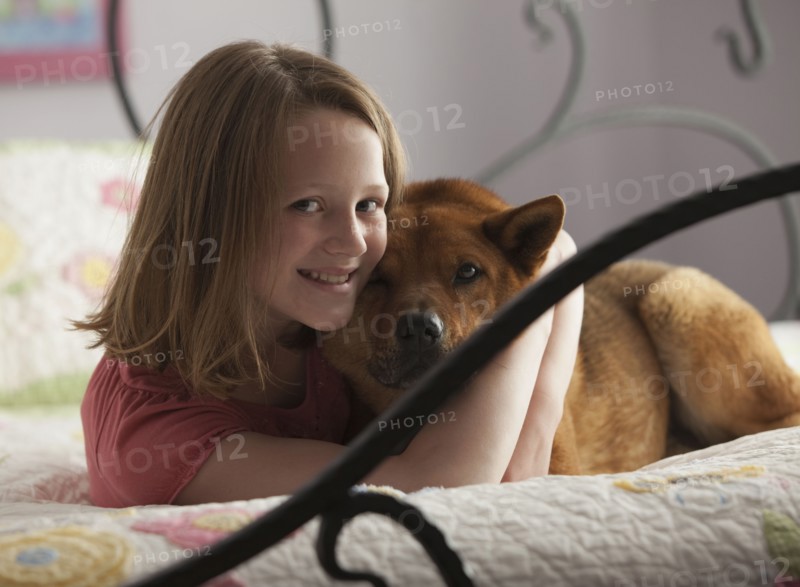 Young girl hugging dog on bed. Photo : Mike Kemp